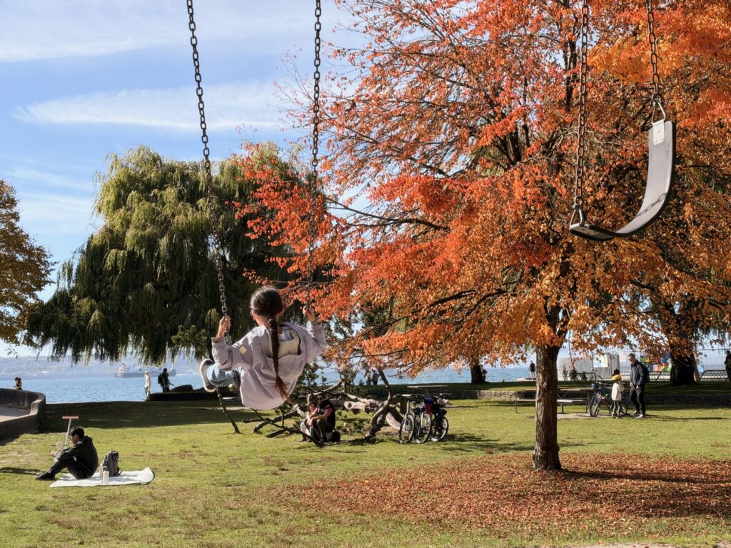 紅葉した木の横で、海を見ながらブランコに乗る子ども