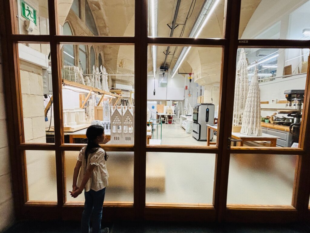 地下の博物館で、ガラス越しに模型の工房をのぞく娘。白い塔の模型が並んでいる