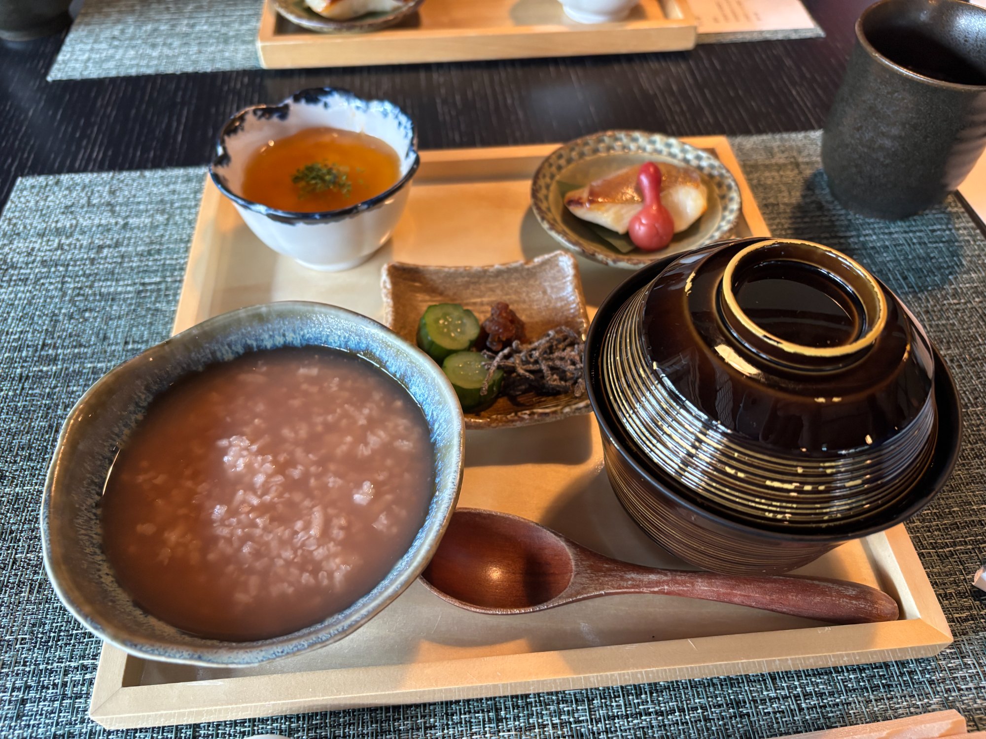 翠葉の朝食。茶粥と小鉢、焼き魚、漬物、蓋つきのお椀がお盆に並ぶ
