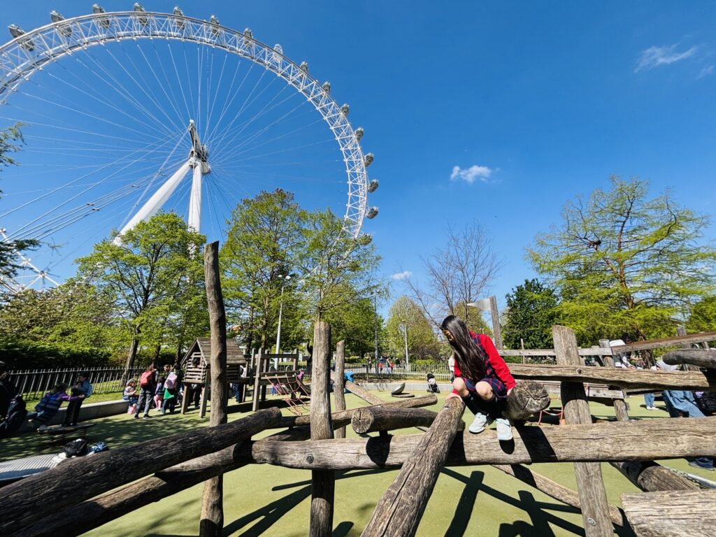 ロンドン・アイの下の公園で、木の遊具に登る娘